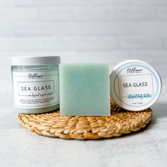 Two containers and a bar of soap labeled 'Sea Glass' on a woven mat with a light gray background.